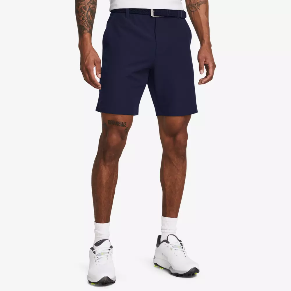 A man wearing navy blue shorts, a white belt, white socks, and white athletic shoes stands against a plain white background. His crisp white shirt is tucked in—styled perfectly for golfers searching for the best golf travel bags. Only his lower body is visible.