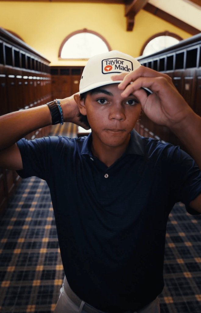 A young boy in a TaylorMade hat in a locker room.