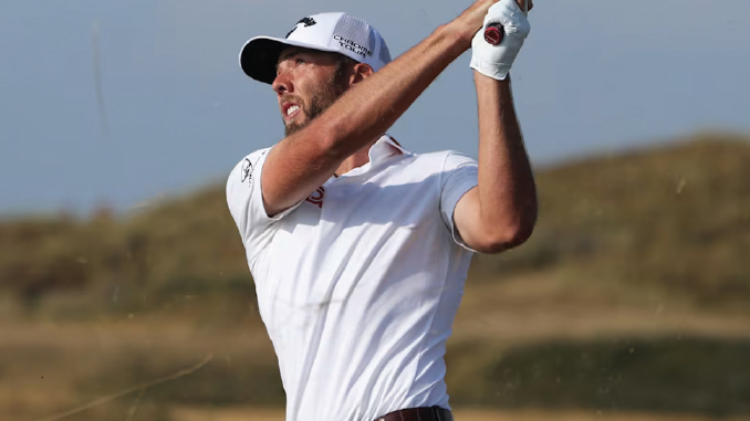 Male golfer in a white polo shirt and cap mid-swing on a golf course, follow-through with a raised club.