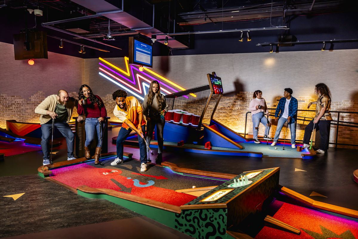 A group of people playing minigolf on a brightly colored course, with others standing in the background waiting their turn.