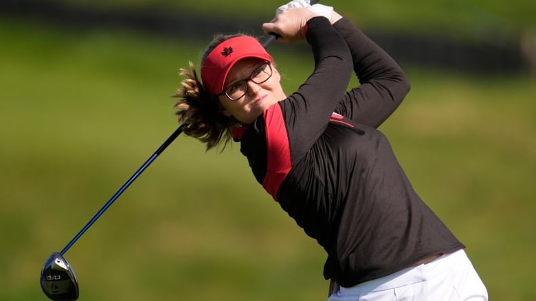 A female golfer is seen from up close after hitting a ball.