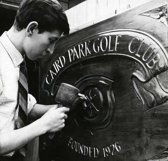 a man inscribes the insignia on a wood and metal sign bearing the name Caird Park golf course