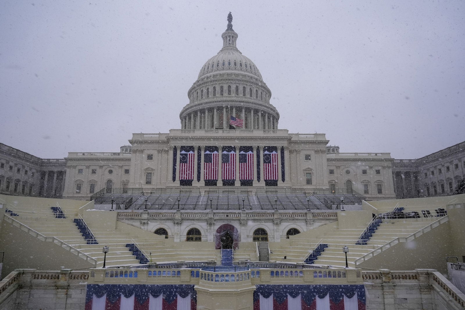 The US Capitol building, draped with US flags, against a snowy backdrop.