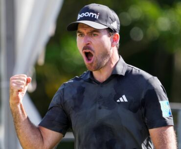 Nick Taylor pumps his fist in celebration while wearing a grey golf shirt and hat