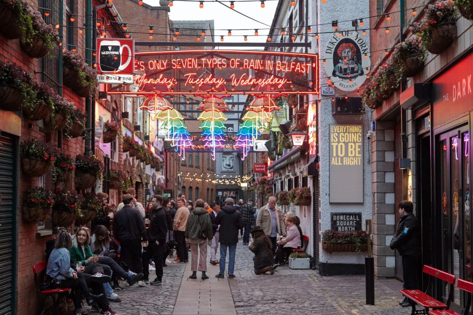 Group of people holding Guinness pints in a Northern Ireland alleyway decorated with colorful umbrellas.