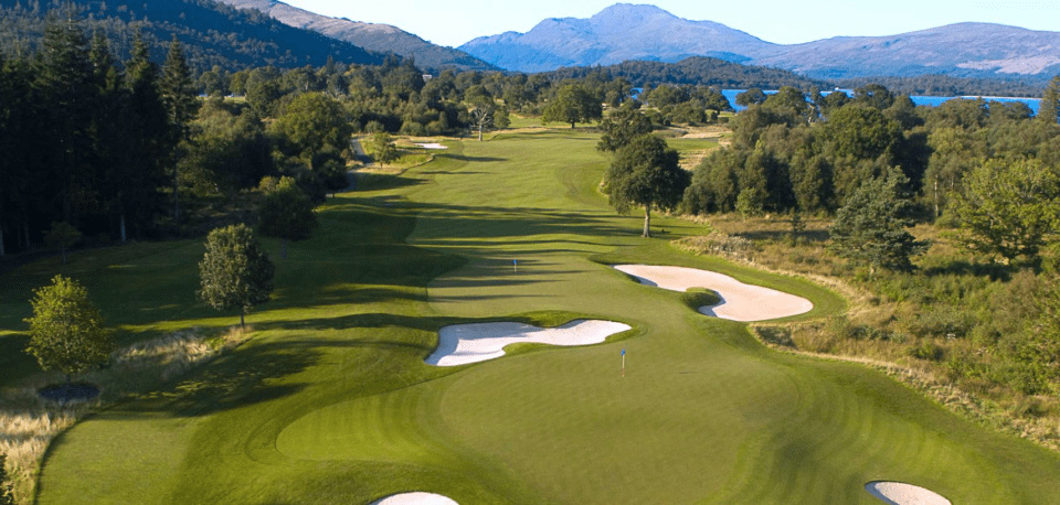 Aerial view of a golf course with sand traps and mountains in the background.