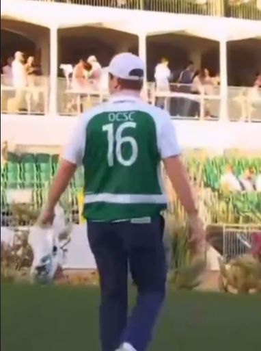A person in a number 16 jersey carrying trash bags walks away from the stands of a stadium.