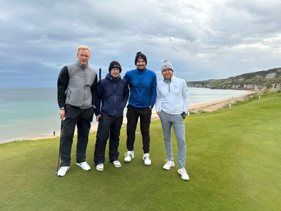 Four men on a golf course by the ocean.