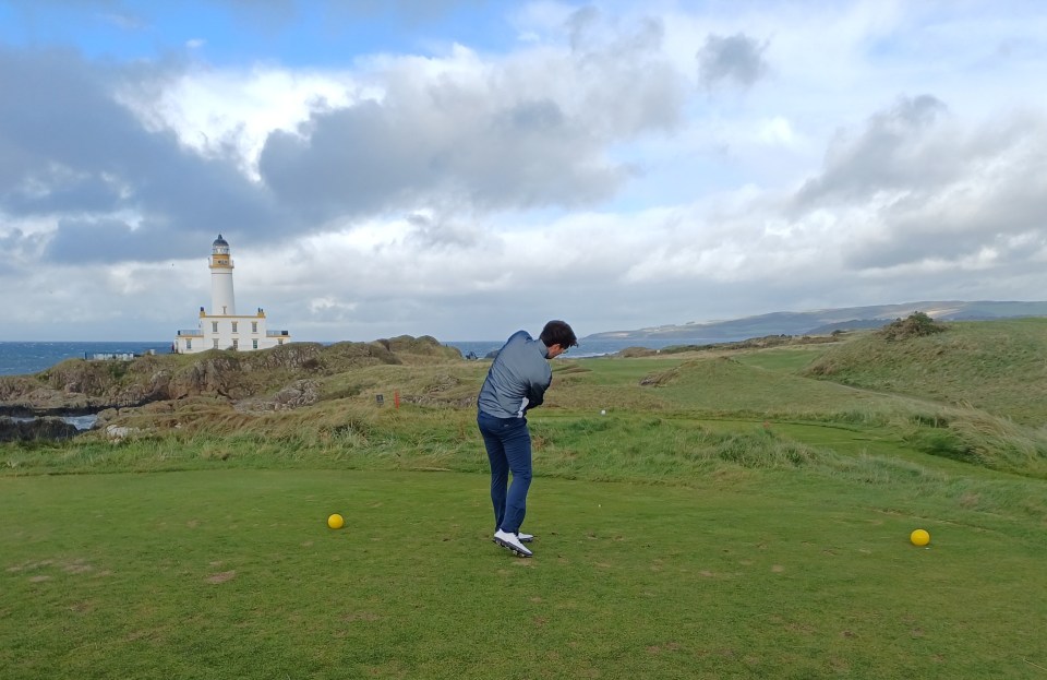 Golfer teeing off on a golf course near a lighthouse.