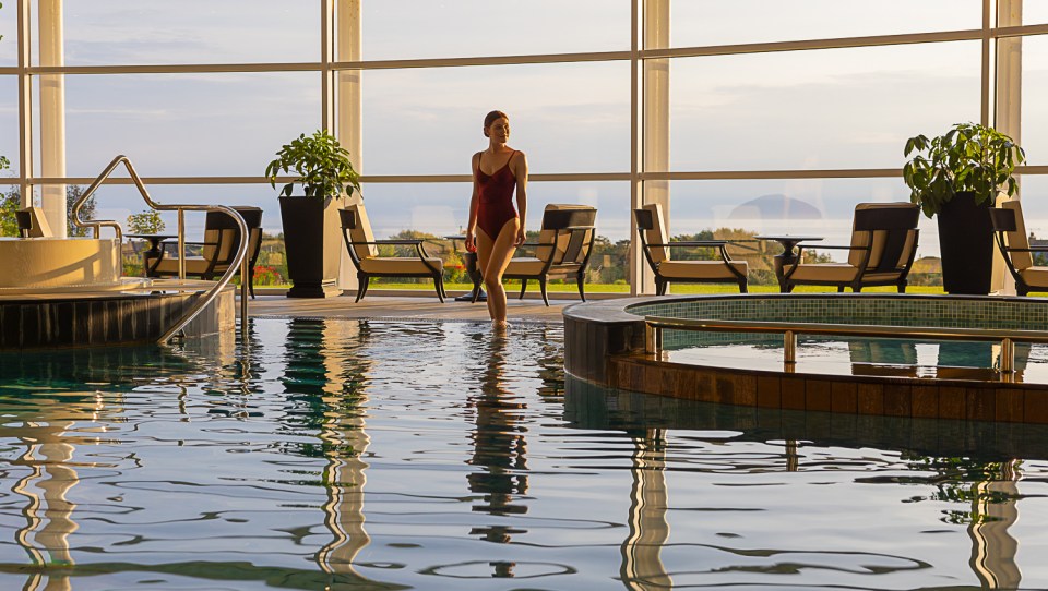 Woman in a red swimsuit walking through a resort pool.