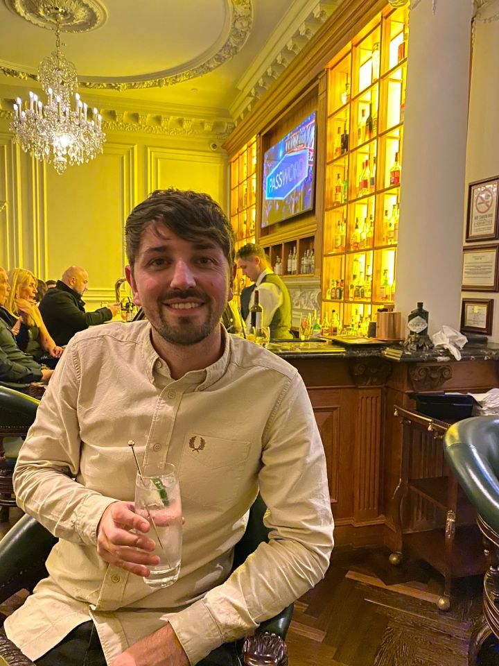 Man holding a gin and tonic at a bar.