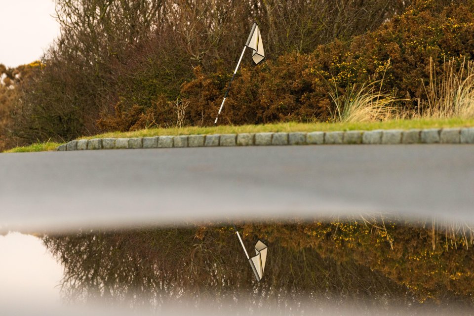 Golf flag on a course reflected in a puddle.
