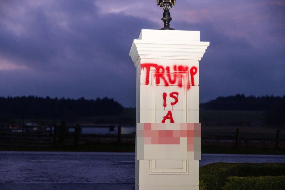 Graffiti reading "Trump is a" spray-painted on a white pillar.