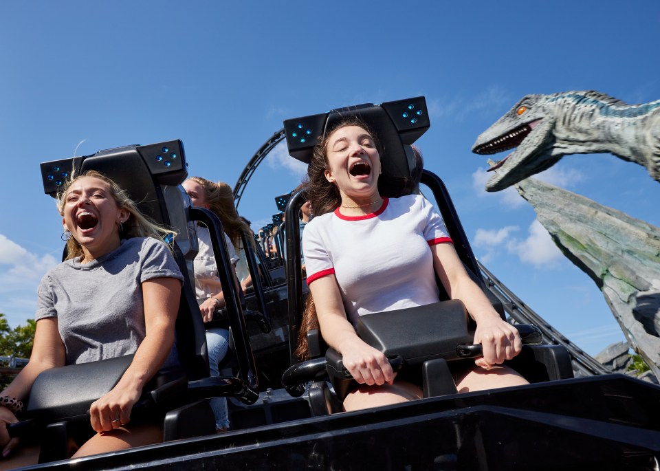 People screaming on a roller coaster with a dinosaur in the background.