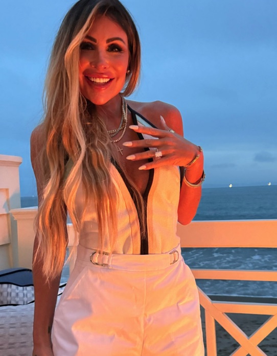 Woman in white jumpsuit showing off engagement ring.