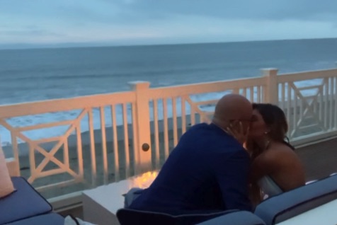 Couple kissing on a deck overlooking the ocean.