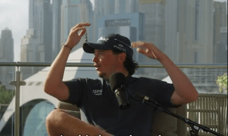 Man in golf cap adjusts his hat while speaking into a microphone.