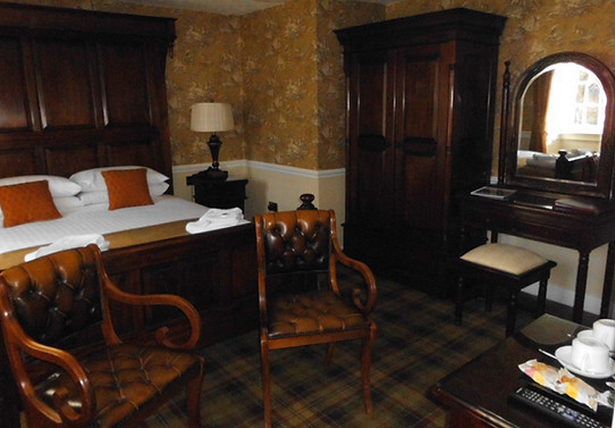A bedroom in The Tweeddale Arms, with a double bed, two chairs, and a wardrobe on a tartan carpet