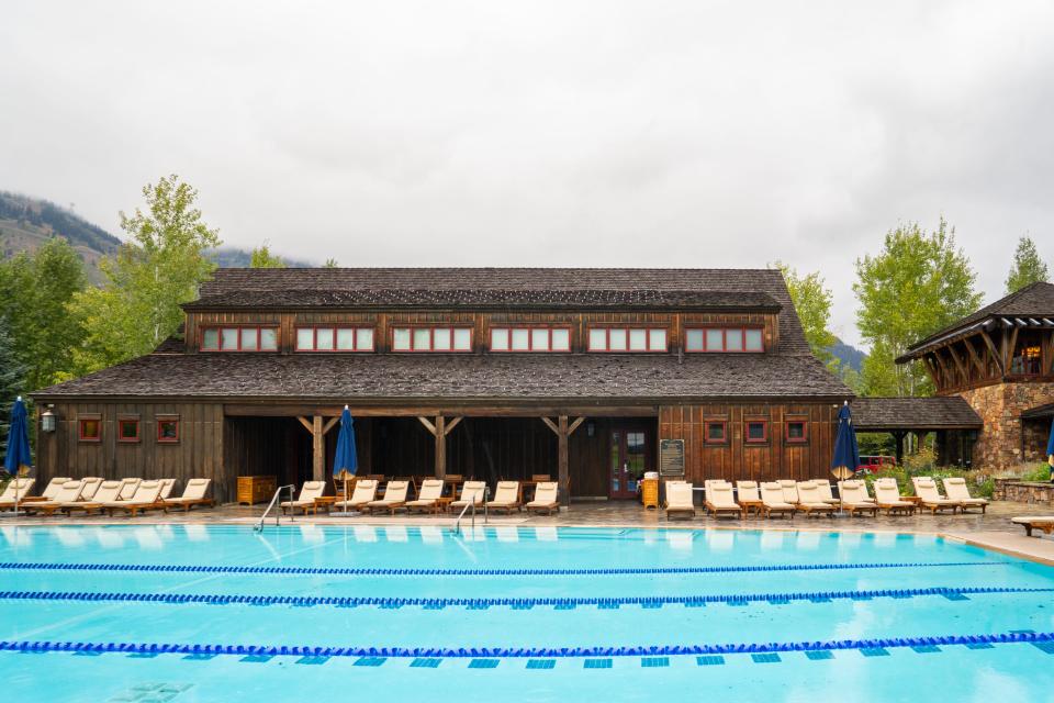 A long, booden barn behing a deck with lounge chairs and a large lap pool