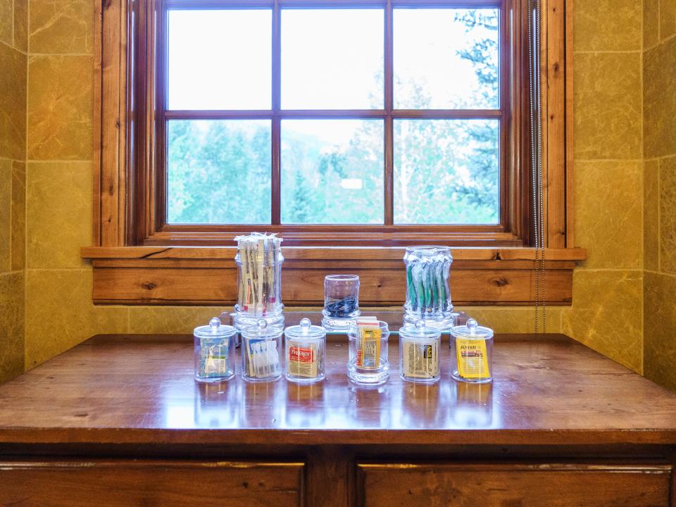 An array of bathrookm amenities in glass jars on a wood table in front of a window
