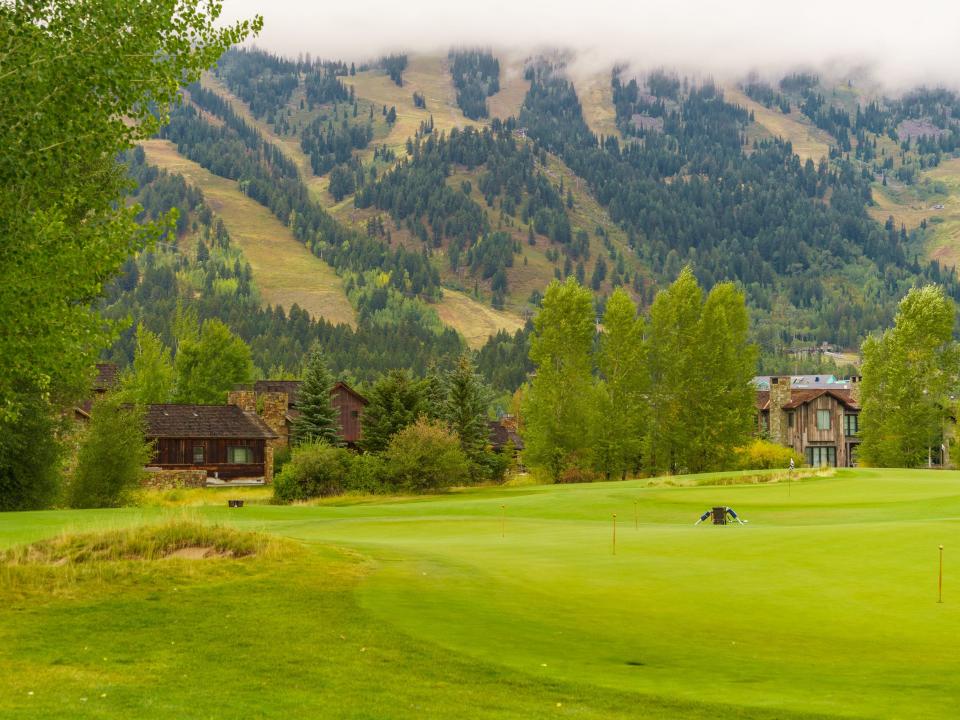 Wood homes behind a golf course with a mountain and a hazy cloud in the background