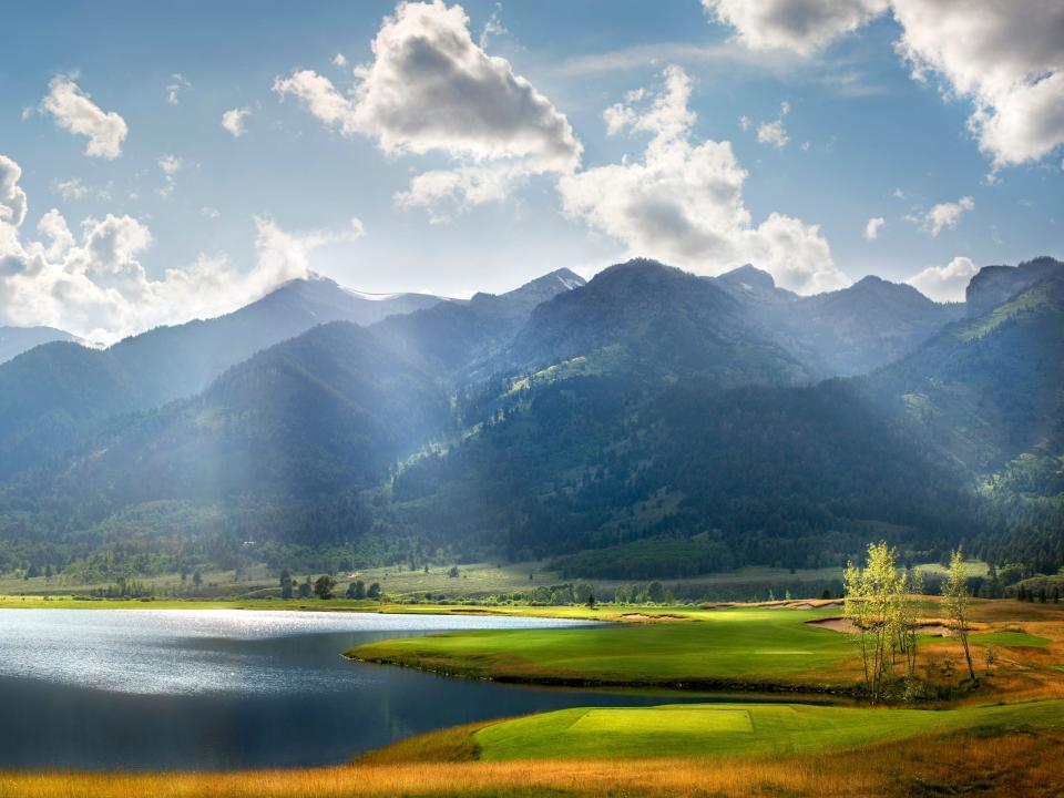 A golf course with a lake on the left, a golf course on the right, and mountains in the background