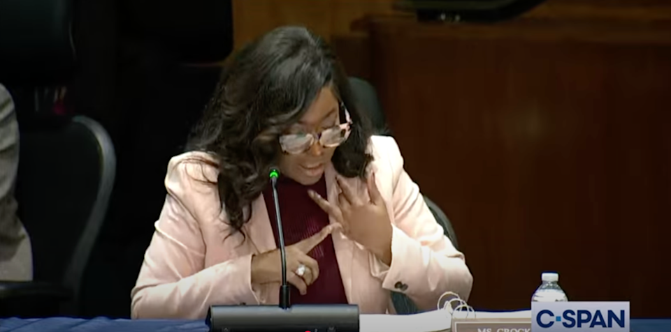 Person speaking at a C-SPAN televised event, sitting at a table with a microphone