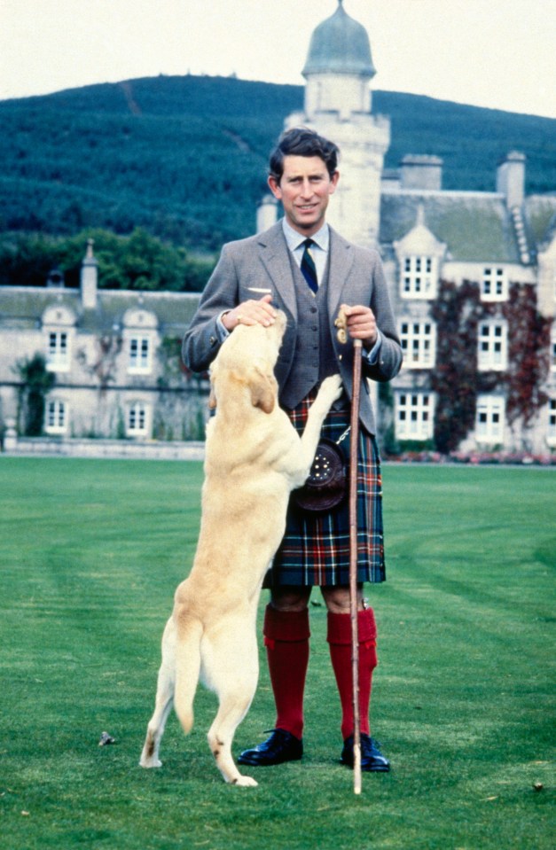 Prince Charles in a kilt petting a retriever at Balmoral Castle.