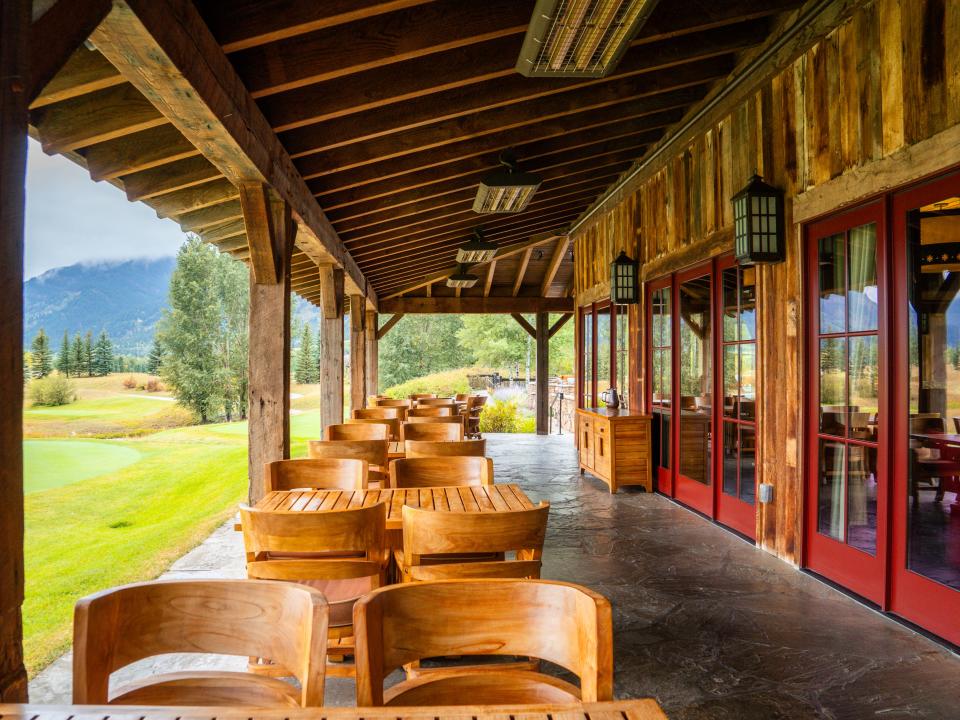 A covered outdoor patio with wooden tables and chairs and a mountain scene on the left an in the background