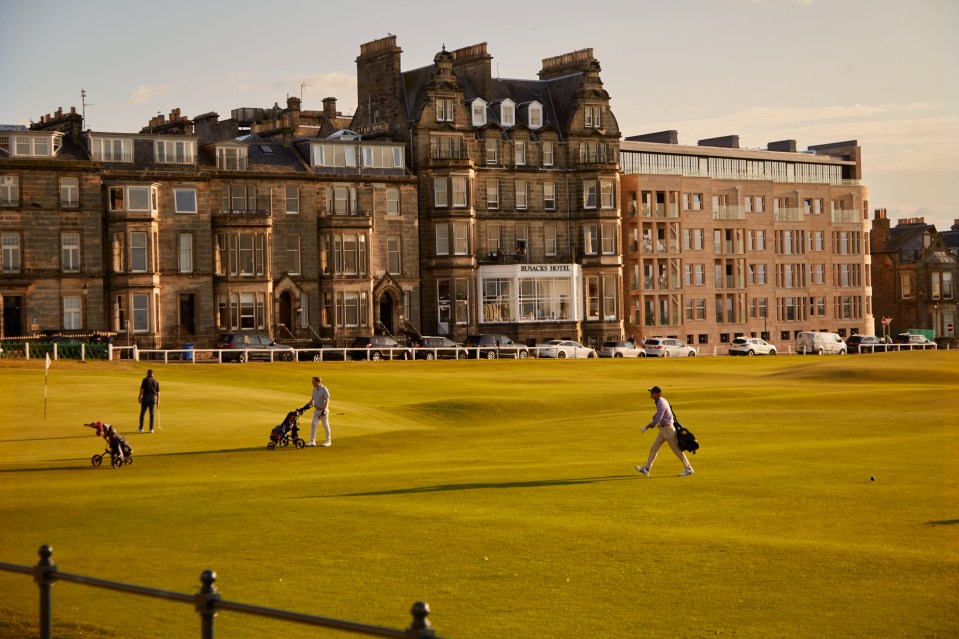 Golfers on a course with the Rusacks Hotel in the background.