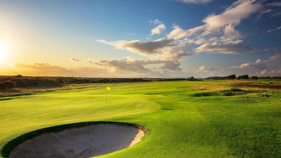 Golf course green with sand trap and flag at sunset.