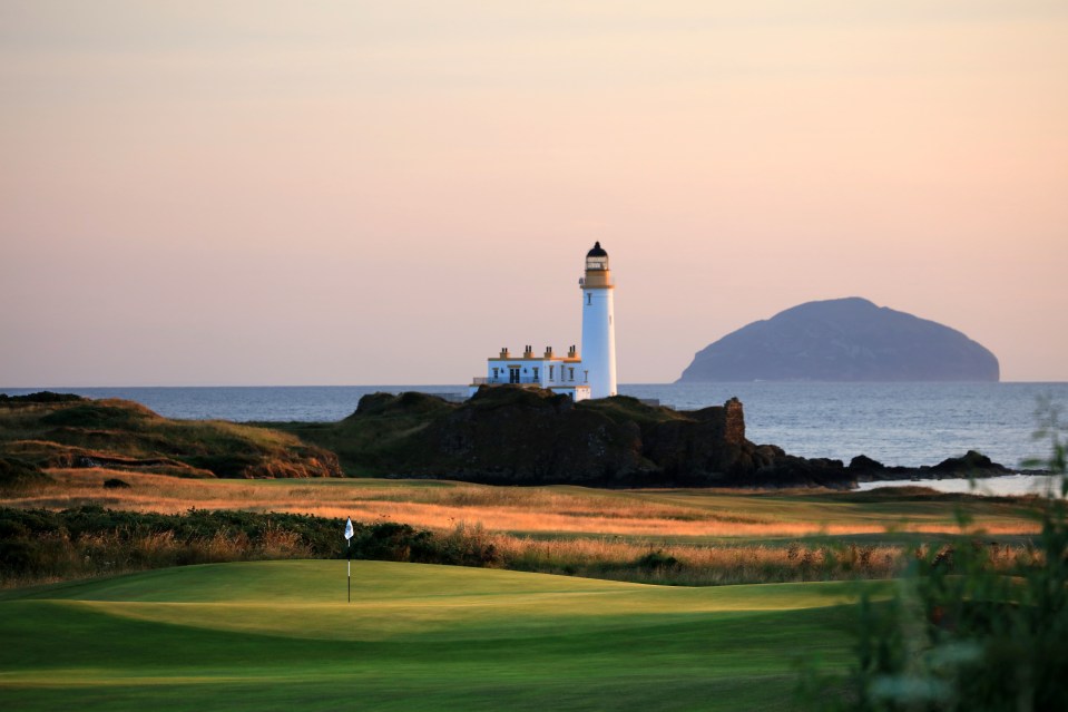 Golf course green with lighthouse and island in the background.