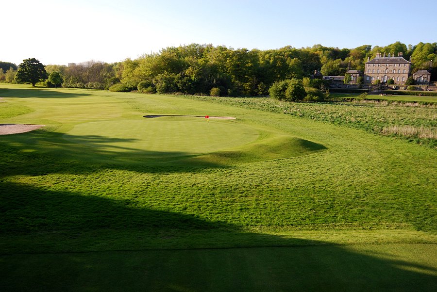 Golf course green with a mansion in the background.
