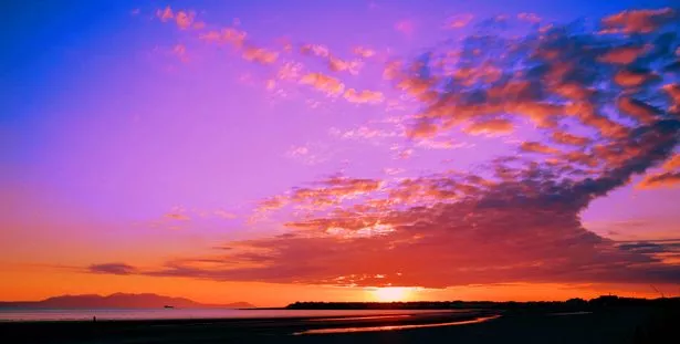 A sky of pink, blue and orange over the island of Arran and the town of Troon in south west scotland as the sun sets.