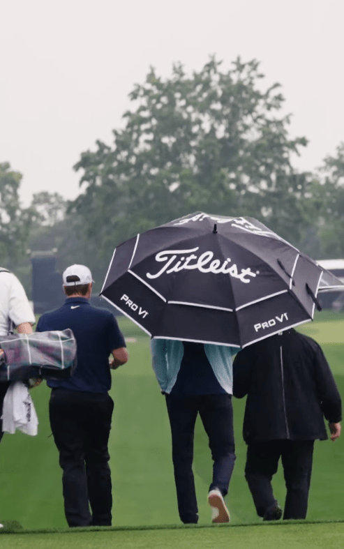 Golfers walking on a course in the rain under a Titleist umbrella.
