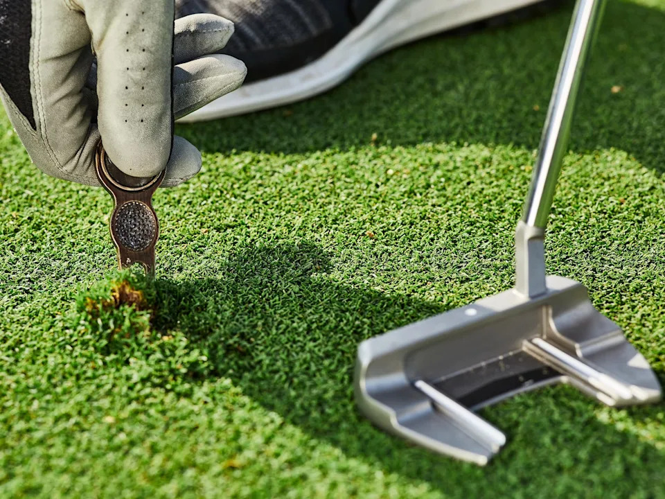 A golfer using a divot tool to repair a nick in the green.