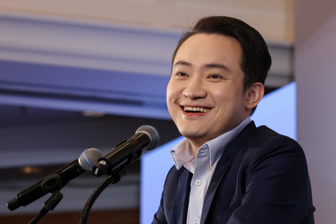 A cleanshaven Asian man smiles while shown in closeup speaking at an event.