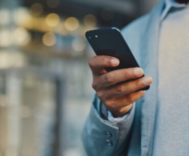 Travel businessman hand with phone in city typing and walking, networking or on 5g mobile app in New York. Street, employee or worker on smartphone for communication or commute to office building (Photo by Layla Bird)