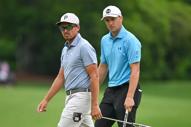 Rickie Fowler and Jordan Spieth walk on the green with clubs in hand