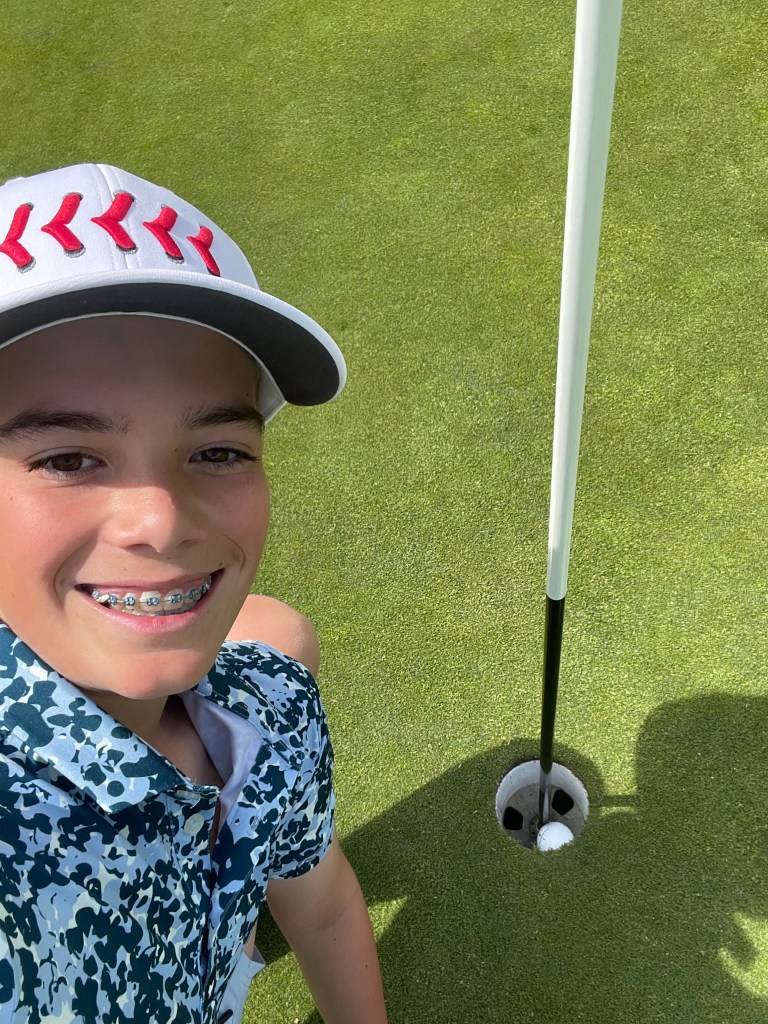 A 13-year-old boy takes a selfie with a hole in one he made on a golf course.