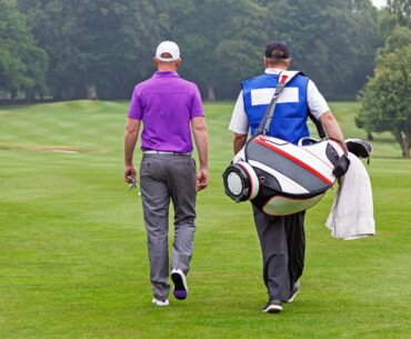 A golfer and his caddie walk across the fairway of a golf course.