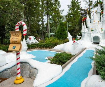 A whimsical Winter Summerland Mini Golf course with a snowy white castle, candy cane sign, and blue water paths.