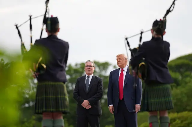 Donald Trump and Keir Starmer stand side by side as bagpipers play.