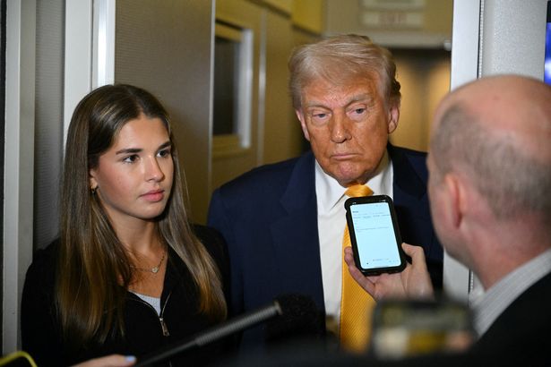 US President Donald Trump listens to reporters as his granddaughter Kai Madison Trump looks on on board Air Force One          
