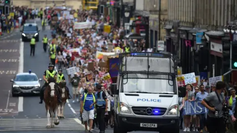Getty Images A Police Scotland van followed by a long protest of hundreds of people in a row. They are carrying anti-Trump banners. They are accompanied by mounted police officers.