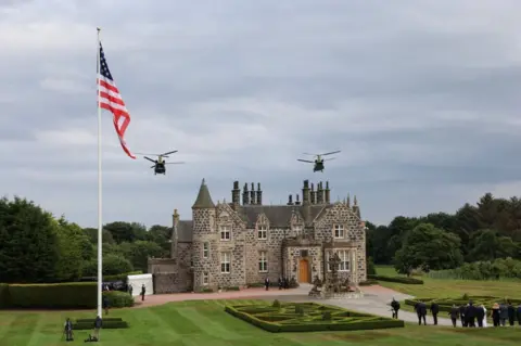 Reuters a small castle building beside a us a flag as two military helicopters fly overhead