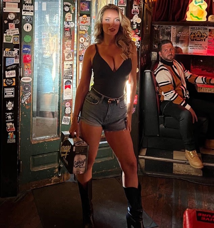 Woman holding beer in a bar with a man in the background.