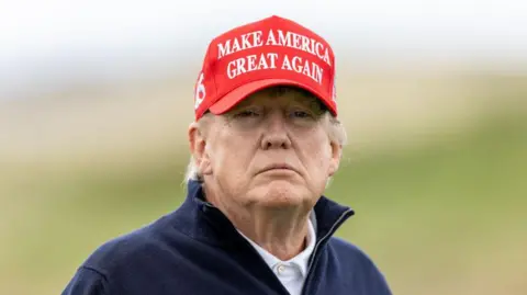 Getty Images Head and shoulders of Donald Trump, who is wearing a white polo shirt, a navy blue fleece and a red cap which says "Make America great again"