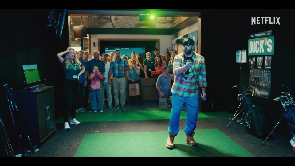 Adam Sandler in a golf simulator, surrounded by spectators.