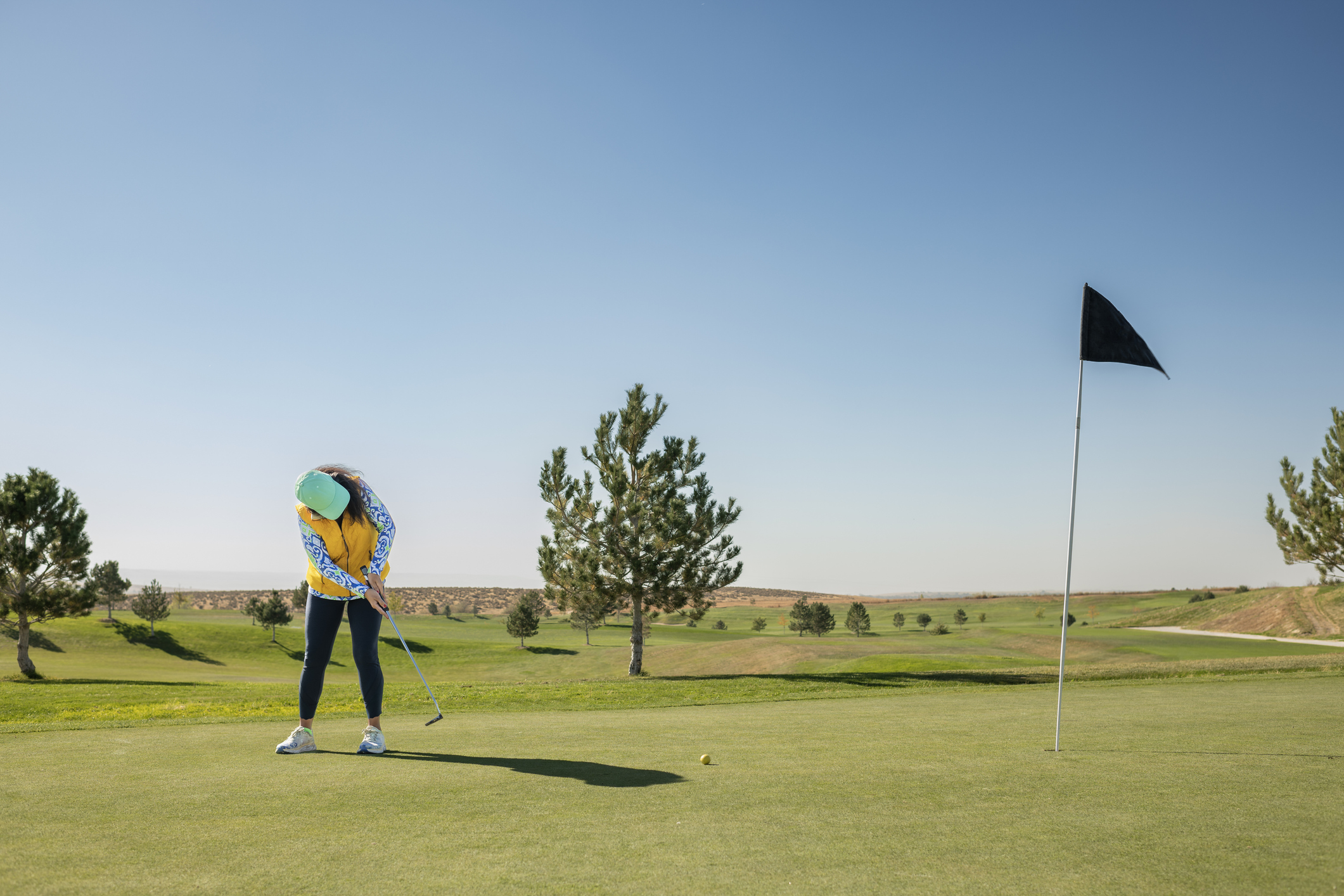 A woman in colorful clothes puts at a golf course.